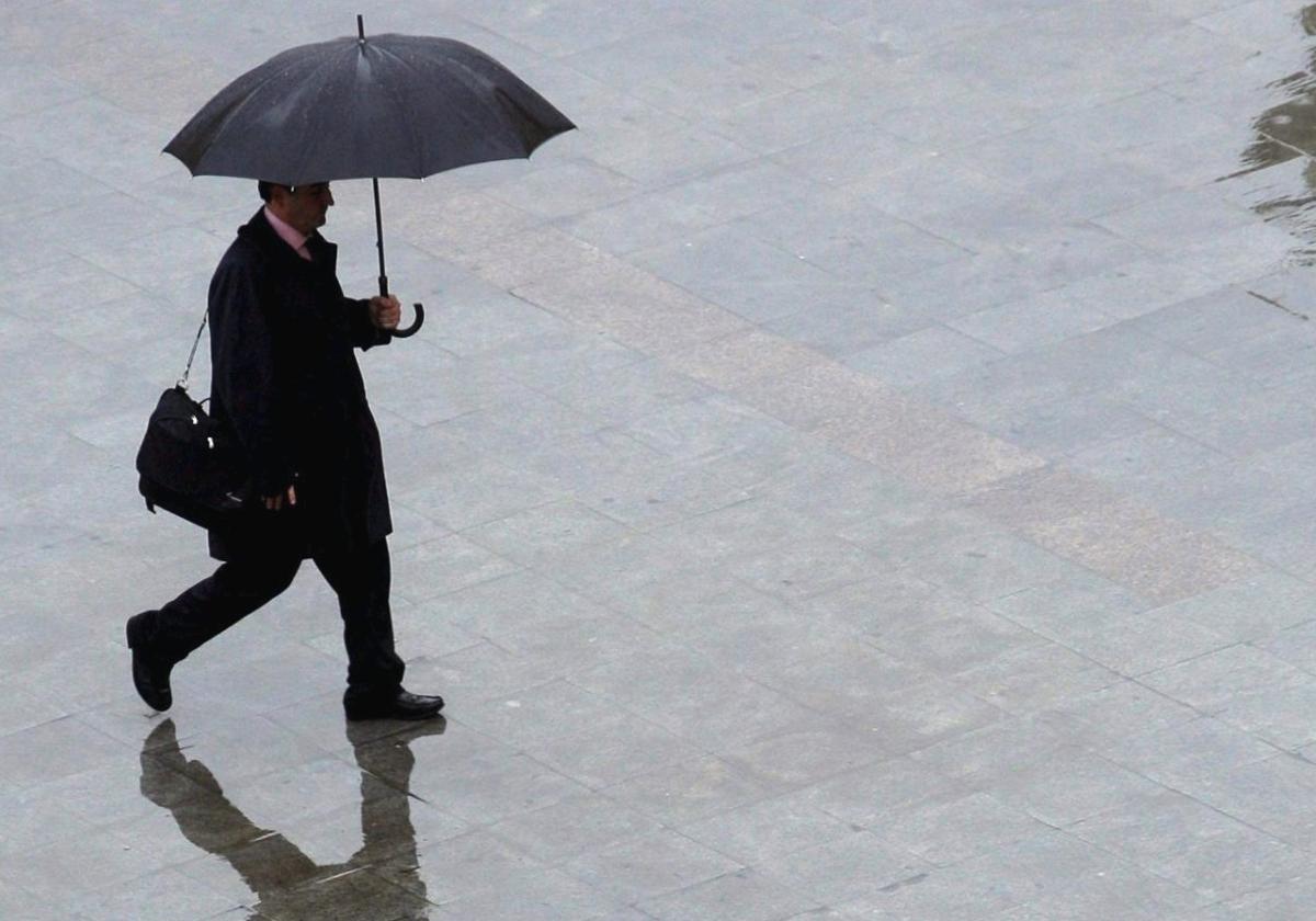 Imagen de archivo de una hombre resguardándose de la lluvia con un paraguas.