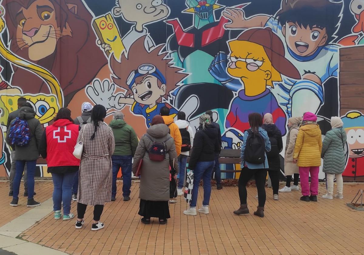 Varios inmigrantes observan el mural de la Lastra.