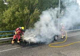 Bomberos de León trabajan apagando las llamas en el coche calcinado.