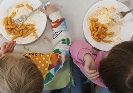 Dos niños comen un plato de macarrones en un comedor escolar.