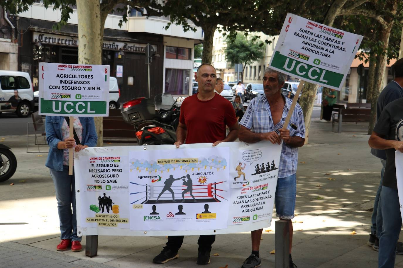 Tres personas sujetan una pancarta que representa una pelea en el ring entre Agroseguro y los agricultores con Enesa y el Ministerio de Agricultura como jueces del combate.