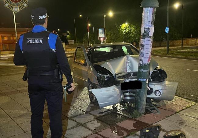 Un agente de la Policía Local de León junto al coche siniestrado.