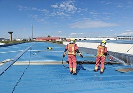 Dos bomberos sofocan el incendio en el tejado de la nave.