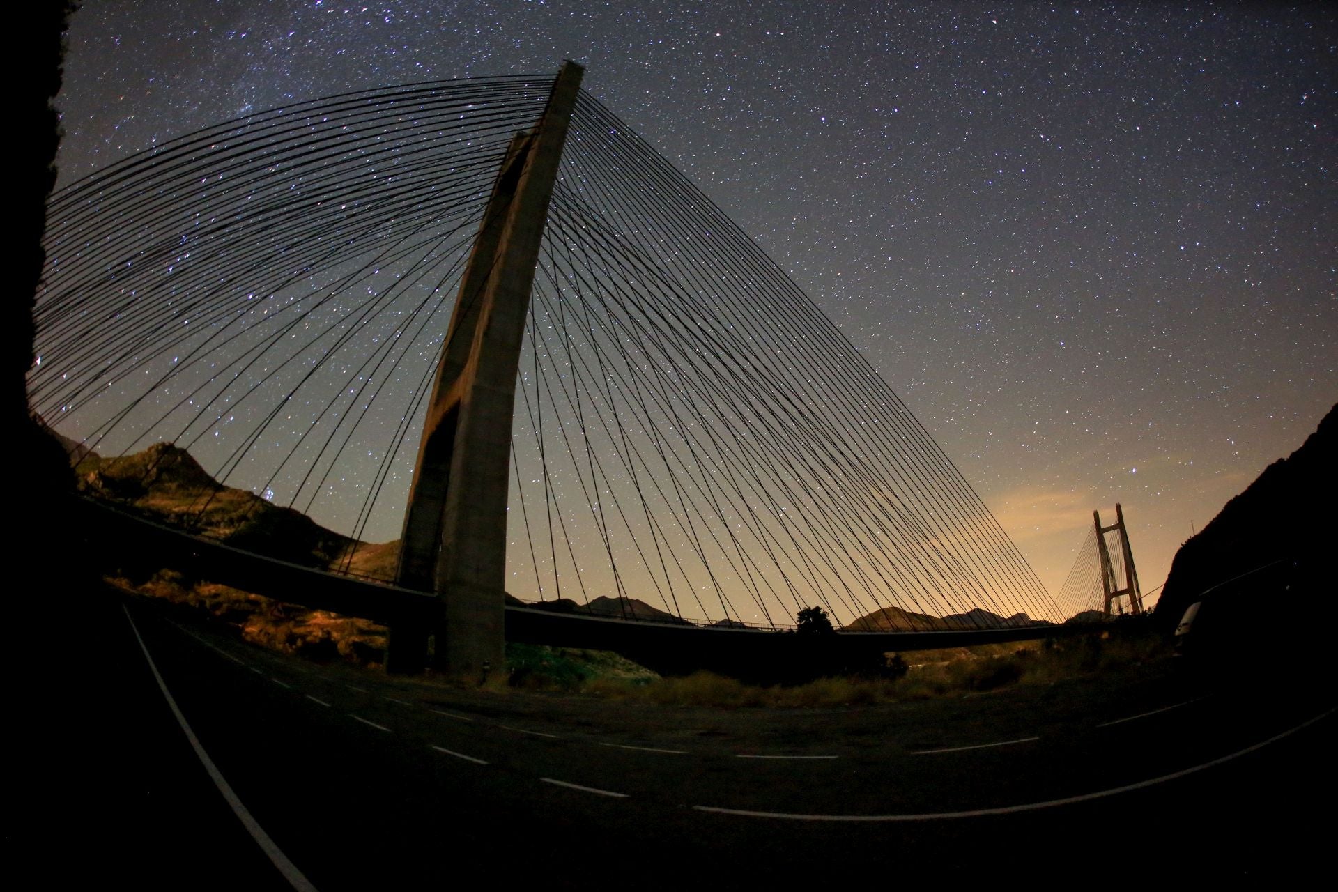 Una espectacular vista del puente de Barrios de Luna y el cielo estrellado durante un atardecer.
