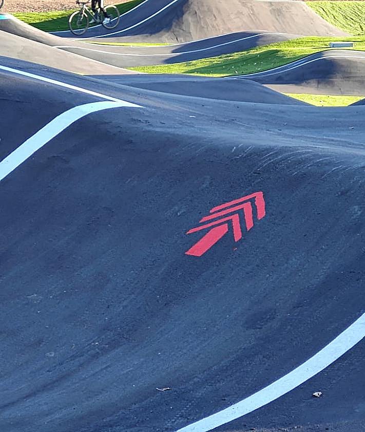 Imagen secundaria 2 - Cartel con las obligaciones de los usuarios; marca que anuncia la colocación de un dispositivo de alumbrado; y una flecha roja que indica la dirección y la dificultad -avanzada- de esta parte de la pista de pumptrack en Puente Castro.