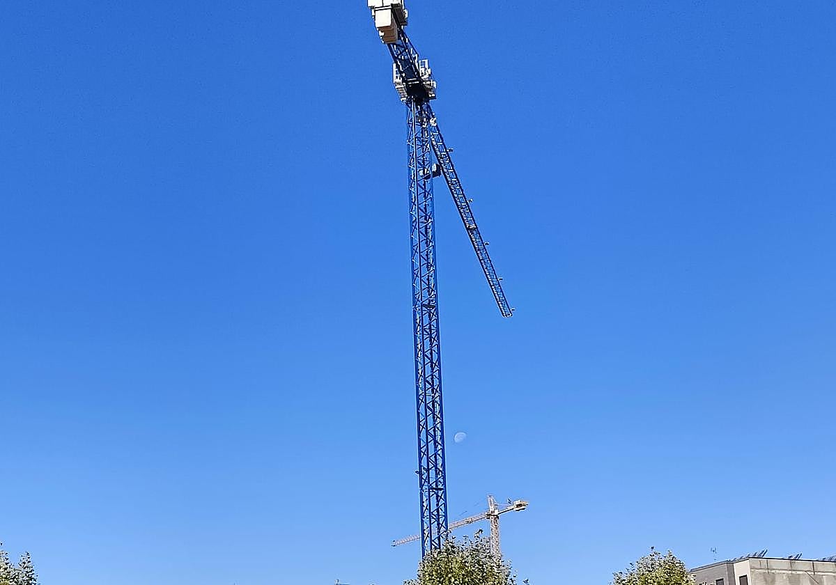 La Luna asoma entre dos grúas de construcción en el barrio leonés de La Lastra.