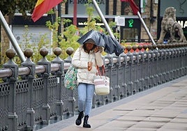 Una mujer lucha contra el viento y la lluvia al cruzar el Puente de los Leones en octubre de 2024, durante el paso de la borrasca Kirk.