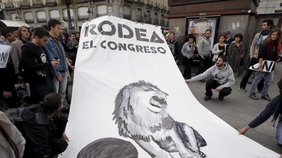 Unos jóvenes despliegan en la Puerta del Sol de Madrid un cartel con el lema 'Rodea en Congreso'.