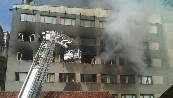 Los bomberos tratan de sofocar las llamas desde una escala.