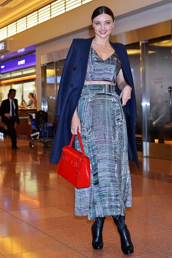 La modelo se pasea por el aeropuerto con un look de dos piezas, falda maxi y top, y abrigo elegante azul sobre los hombros.