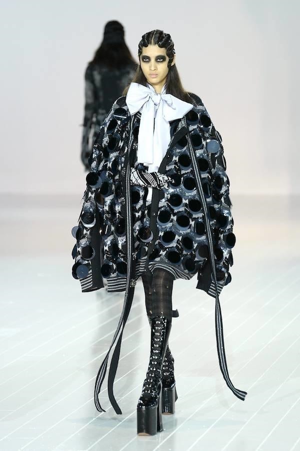 Impresionante capa 'sportif' con elástico y adornos en círculos, sobre camisa blanca con lazada gigante.