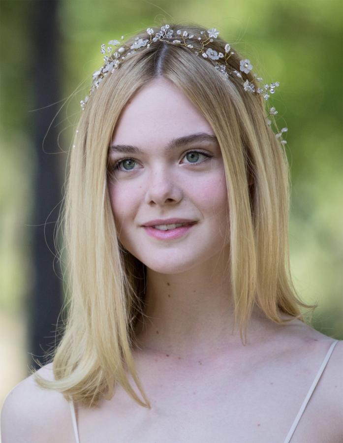 Elle Faning con su melena suelta con raya en medio, adornada con una delicada diadema de flores.