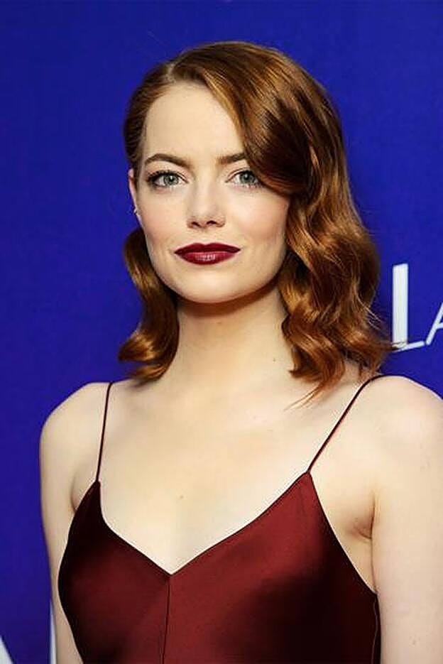 Emma Stone, en plena promoción de La La Land con media melena semirrecogido y ondas marcadas, y labios vamp, en color granate.