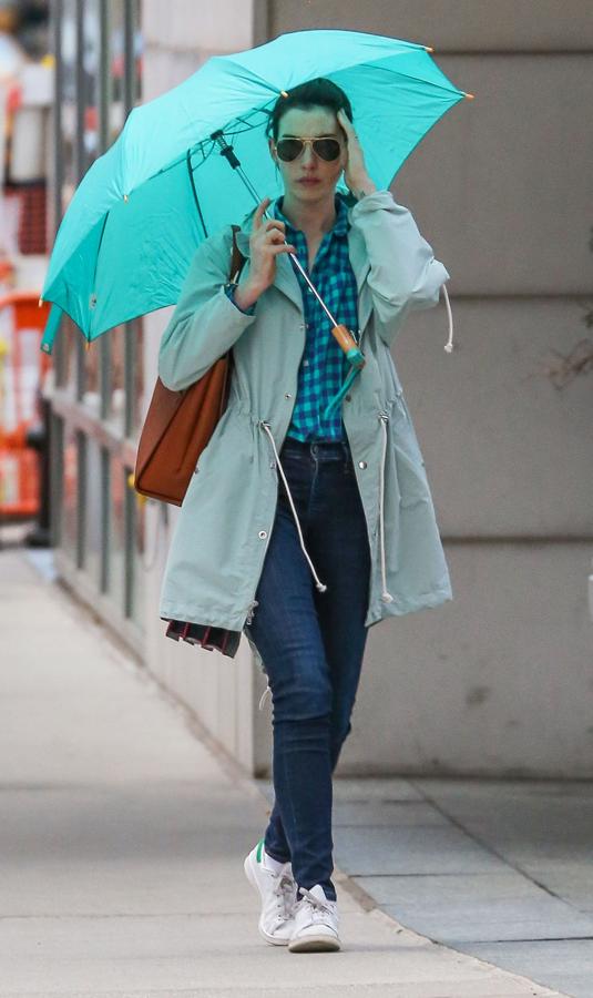 Anne Hathaway con chubasquero, camisa y paraguas en color azul, todo a juego con unas Stan Smith blancas con detalle en el mismo color.