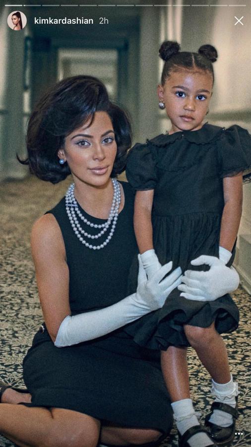 Kim Kardashian con su hija. Las dos con un vestido negro y guantes blancos. Kim, con un collar a perlas largo.