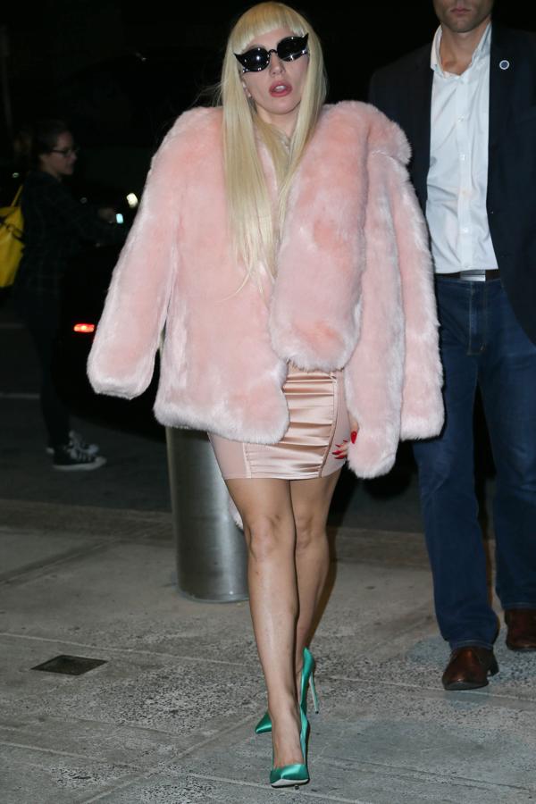 Lady Gaga en JFK. Lleva un vestido rosa palo y un abrigo de pelo del mismo color. Lo acompaña de unos zapatos de tacón verde eléctricos.