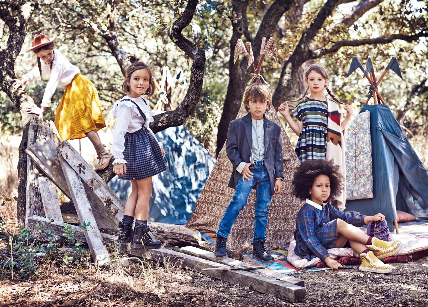 En lo alto del árbol, Stella lleva camisa de Mango Kids, falda amarilla de Thanks Mum, calcetines de Cóndor y zapatos de Primark. Valeria luce camisa con chorreras de Gocco, pichi de Mi pequeño Lucas, calcetines de Cóndor y zapatos de Primigi. Roberto ha elegido zapatos de Hugo Boss, camisa y pantlón de Primark y botas de Garvalín. Stella luce vestido de rayas de Armani Junior. Sentada, Paula lleva vestido de Bonnet á pompon, calcetines de Calzedonia y botas de Mou. La mantas, tipis y cojines son de Thanks Mum.