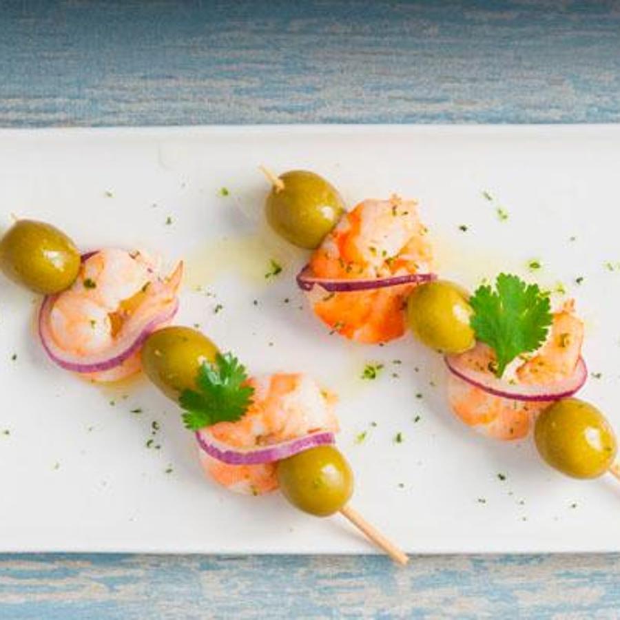 Prepara brochetas con langostinos cocidos (que no tengan mucha sal), cebolla morada, hojas de cilantro y aceitunas verdes carrasqueña. Rocía con zumo de lima.