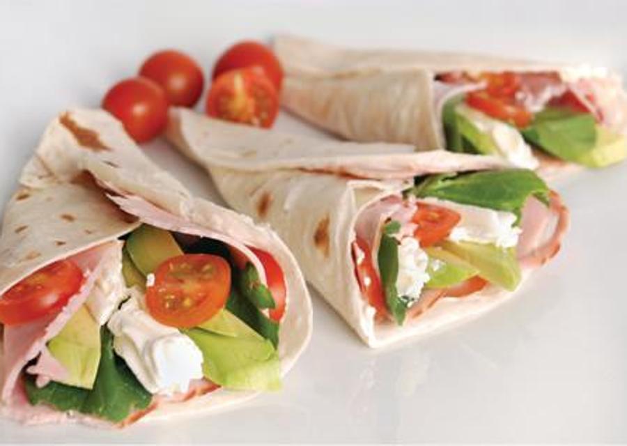 Elabora un rollito con tortitas de wrap integrales, introduce pavo, aguacate, tomates cherry y hojas de rúcula.