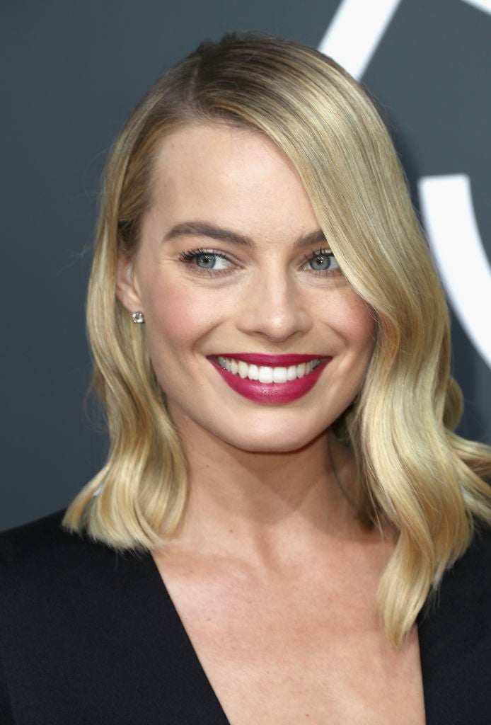 Margot Robbie con su media melena suelta con raya a un lado y ondas abiertas y labios en color rojo cereza.