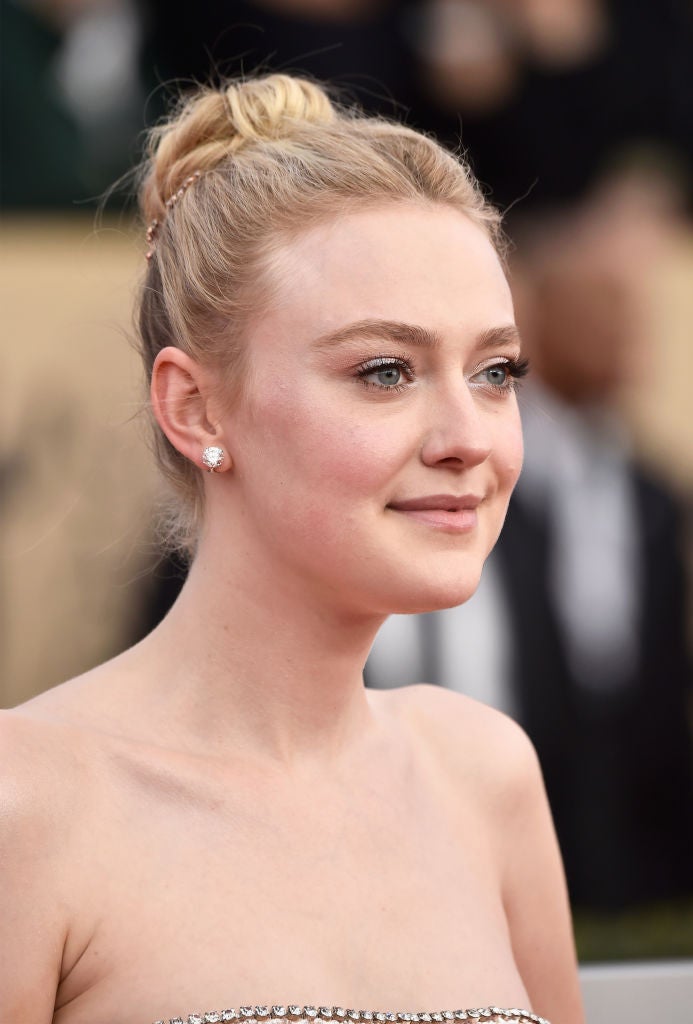 Dakota Faning con un moño de bailarina alto y adornado con accesorio joya, y maquillaje en tonos rosas.