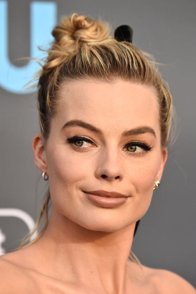 Margot Robbie con su media melena recogida en un moño alto o 'top knot' ladeado y adornado con un lazo negro, el complemento más trendy de la temporada para el pelo.