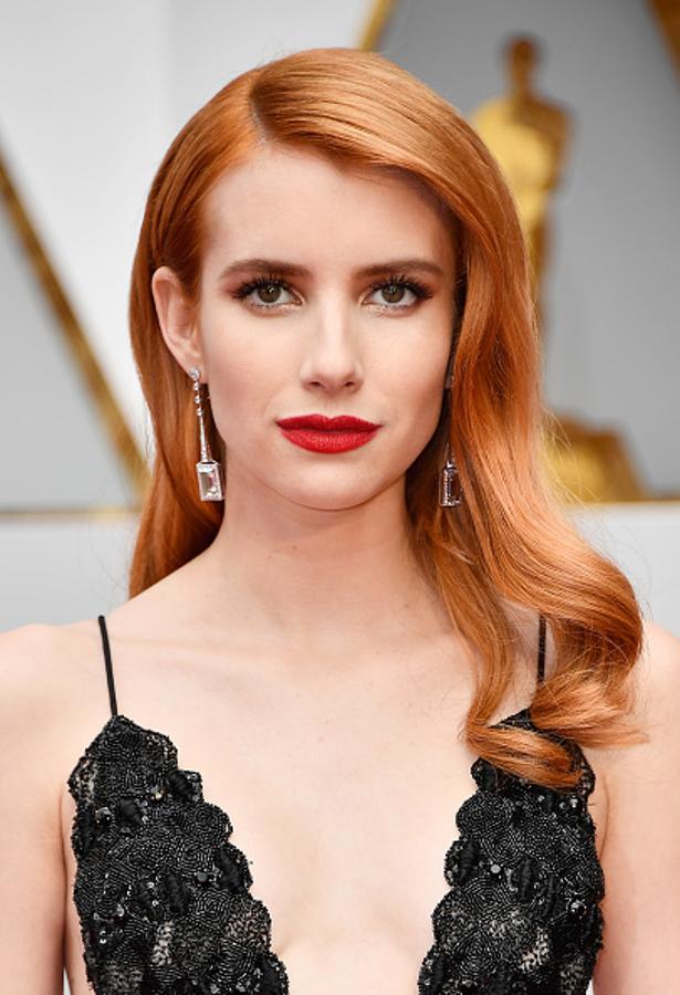 Emma Roberts con melena pulida en las raíces y ondas en las puntas, en los Oscar 2017 y un bonito maquillaje con labios rojos y sombras doradas.