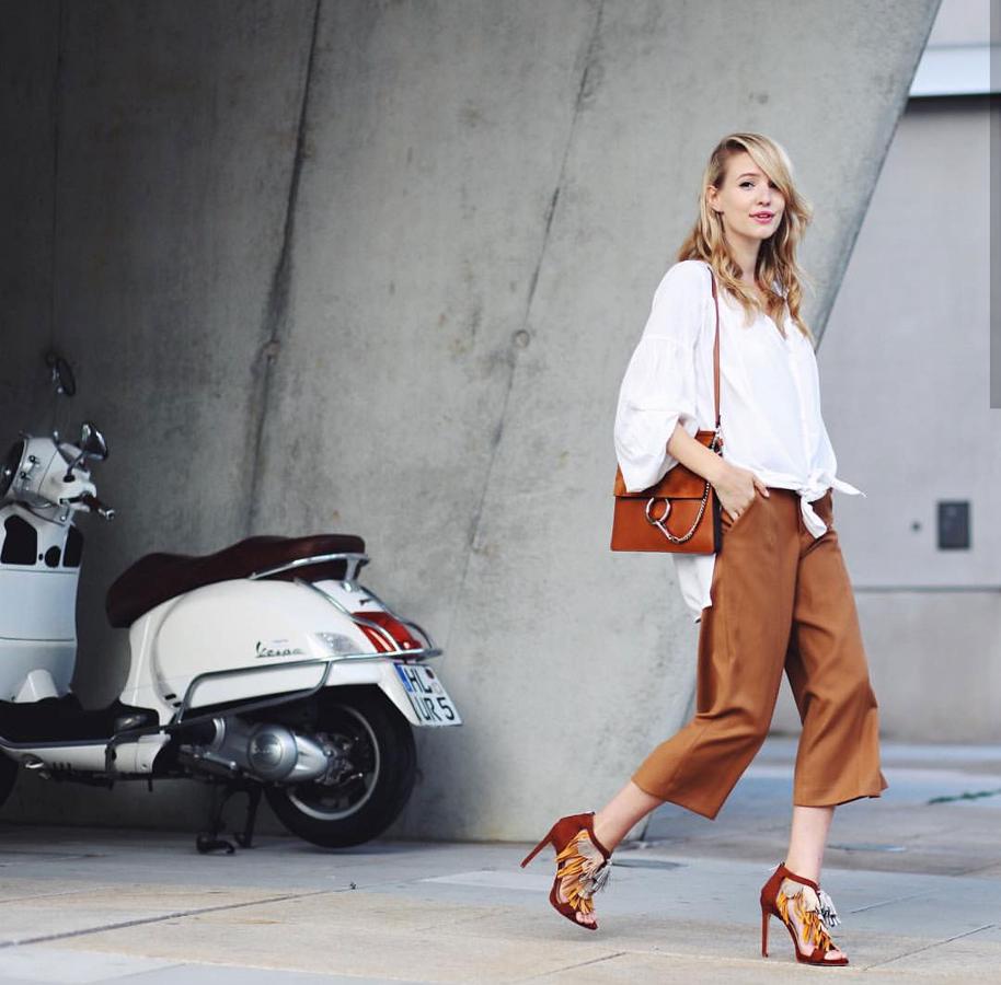 En Instagram, @ohhcouture, opta por estos pantalones de polipiel marrones estilo 'culotte', sandalias de tacón con flecos, blusa blanca anudada y bolso marrón a juego con el 'look'.