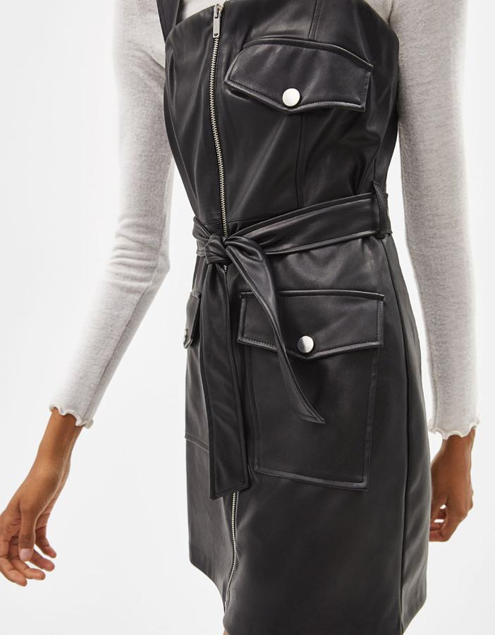 Vestido corto efecto piel con tirante ancho, escote recto y detalle de bolsillos solapa en la parte delantera. Lleva cierre mediante cremallera metálica y cinturón en el mismo tejido (25,99 euros).