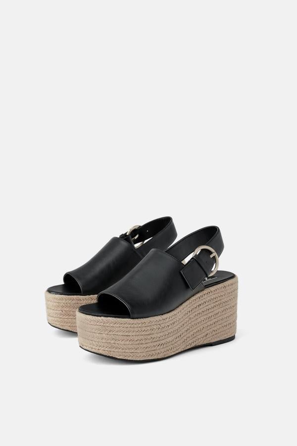 Fantásticas sandalias de color negro, con una tira ancha en la parte delantera y otra por detrás del tobillo, adornada con una hebilla metálica. La cuña con plataforma forrada es de yute (35,95 euros).