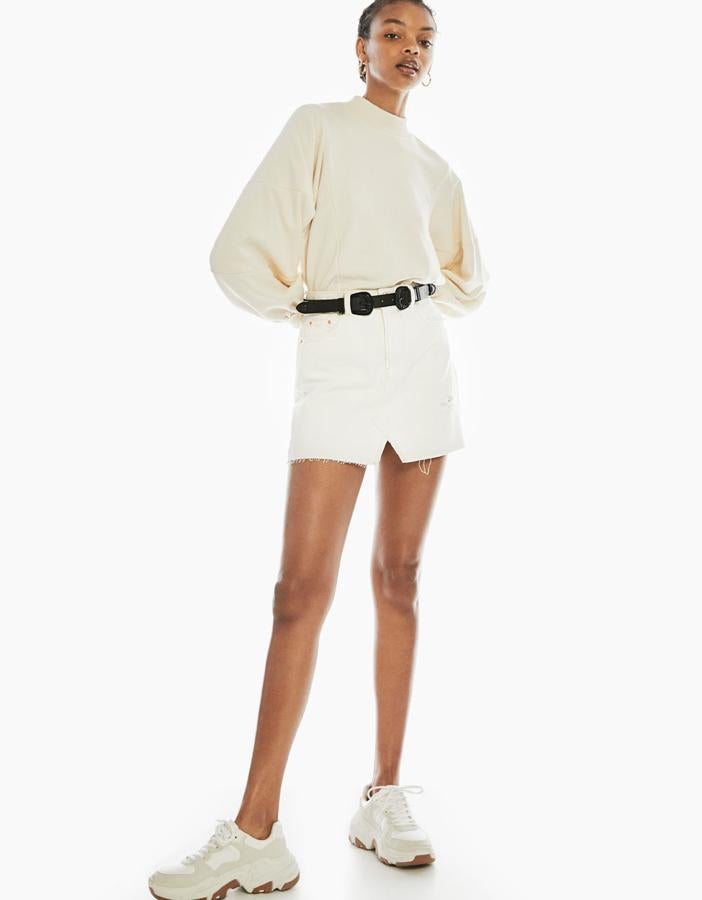 Falda corta en denim con tiro alto, trabillas, dos bolsillos delanteros y pequeña abertura (19,99 euros) combinada con un sudadera 'cropped' con cuello redondo y manga larga, corte holgado, hombro ligeramente caído y bajo cortado a sangre (9,99 euros).