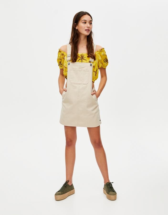 Peto vaquero en color crema  (19.99 euros) y crop top con escote 'off the shoulders' (15.99 euros), todo de Pull&Bear.