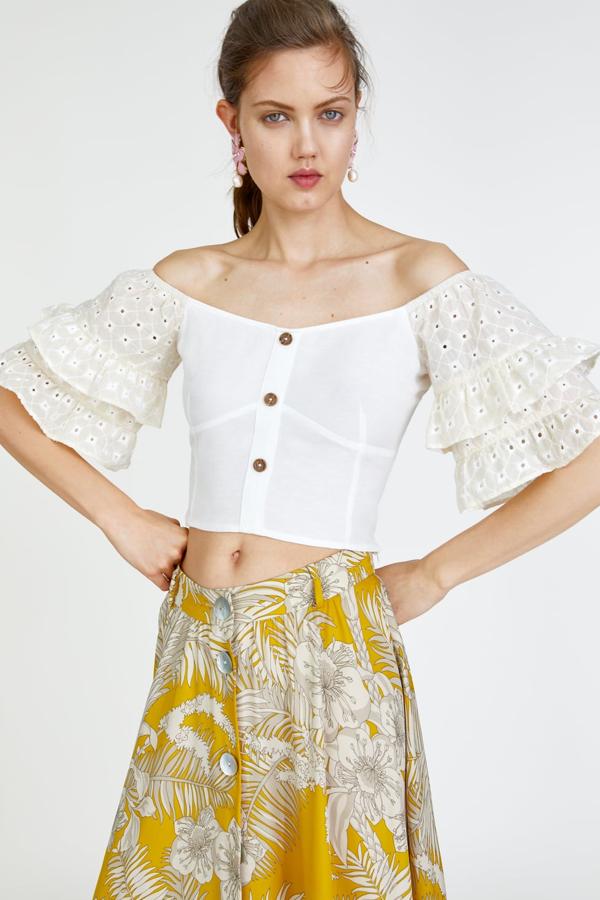 Cuerpo corto con el escote recto y manga corta con volantes, adornados con bordados perforados. lleva un elástico tipo nido de abeja en la espalda y cierra con botones combinados a contraste (25,95 euros)..