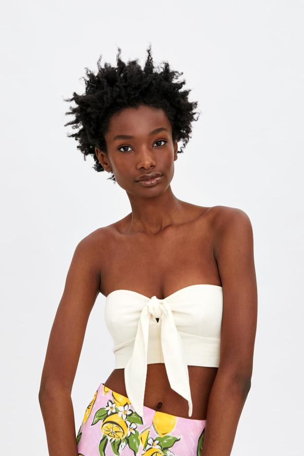 Top corto de escote amplio, con el detalle decorativo de un nudo en el frontal. Lleva un elástico tipo nido de abeja en la espalda (12,95 euros).