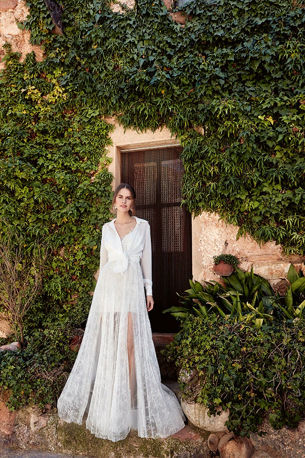 Aunque el segundo vestido de novia y la blusa con la que lo acompañó pertenece a la colección 2018 de YolanCris, la firma nupcial sigue manteniendo en su catálogo looks muy parecidos, como este conjunto de vestido bordado con camisa blanca superpuesta.