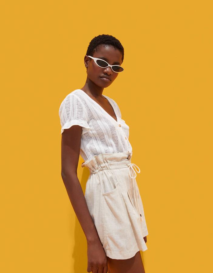 Camiseta con botones blanca (12,99 euros) a contraste con un short de lino beis con cordón, tiro alto, fajín y cordón (17,99 euros).