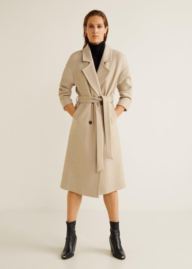 Abrigo de lana con un diseño largo, estructurado y con grandes solapas, con manga larga con puños abotonados, bolsillos laterales, lazo desmontable a la cintura y trabillas y doble botonadura (Mango, 79,99 euros).