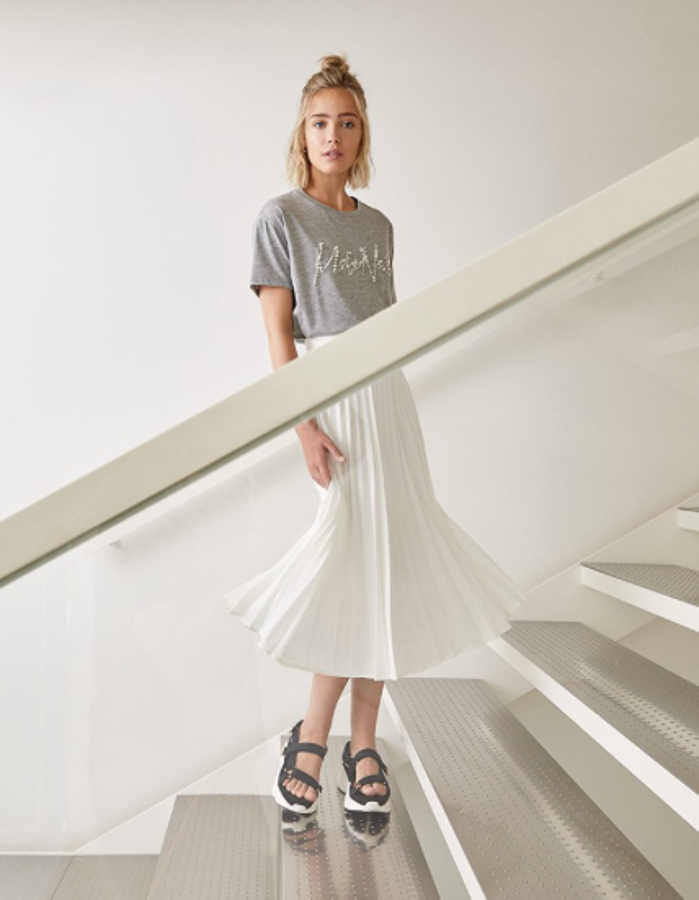 Falda midi plisada con goma en la cintura (25,99 euros), camiseta adornada con un bordado joya (15,99 euros) y sandalias deportivas negras con plataforma de 4,5 centímetros (29,99 euros).