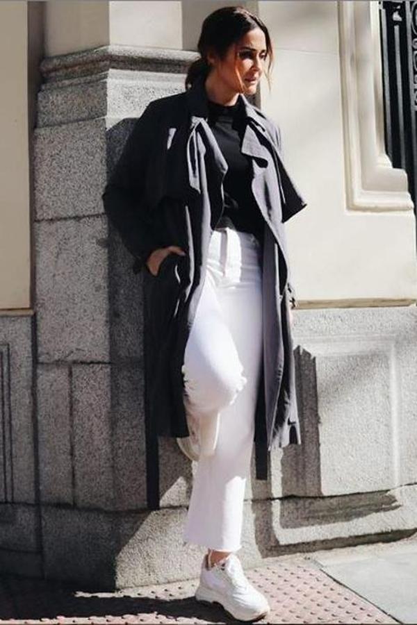 La diseñadora sevillana ha elegido una gabardina de trench en negro, de tejido fluido, que lleva desabrochado para conseguir un look informal. Y lo combina de la mejor manera posible, con dos de los imprescindibles: unos pantalones blancos anchos y de corte al tobillo y unas zapatillas blancas.