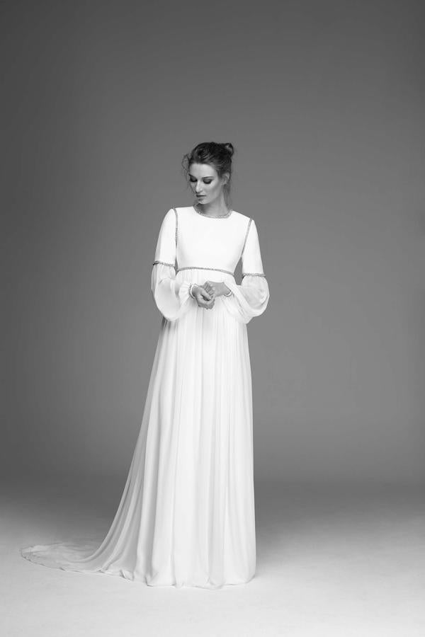 Vestido de crepé y gasa, de corte imperio. Escote a la caja y manga larga con aplicaciones metálicas que hacen las veces de costuras.