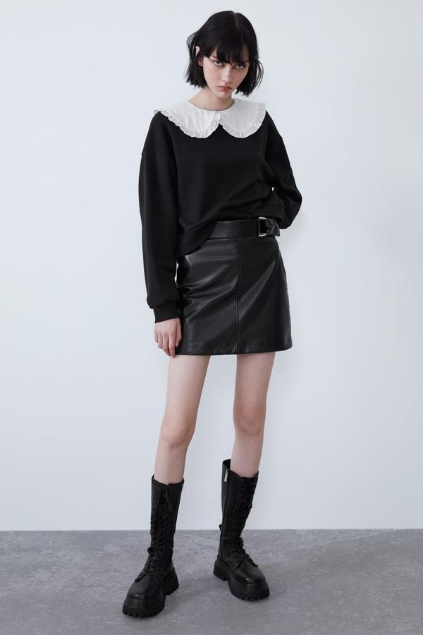 Sudadera corta de cuello redondo, con aplicación de un cuello bobo de color blanco (19,95 euros). Bota plana de piel de color negro con cordones, punta cuadrada y tirador trasero (99,95 euros). Lleva una suela gruesa tipo track y cierra con una cremallera interior. Falda mini de tiro alto con detalle de hebilla metálica, bajo con abertura en la espalda y cierre lateral con cremallera (19,95 euros). Todo de Zara.