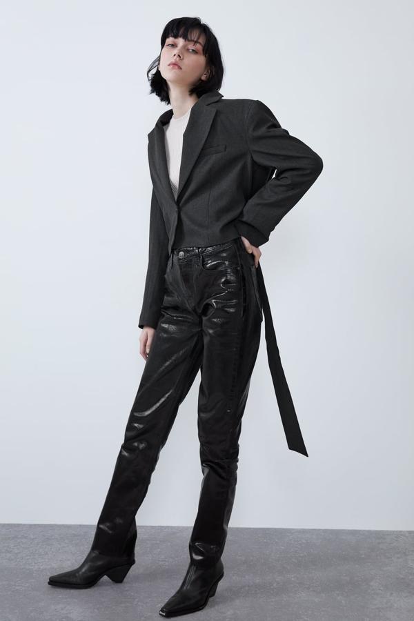 Jeans de tiro alto confeccionados en un tejido con efecto brillo. Llevan la pernera ancha, cinco bolsillos y el bajo acabado sin costura (29,95 euros). Blazer corta con las hombreras cuadradas, falso bolsillo de vivo en el frontal y un cinturón de lazada en mismo tejido (39,95 euros). Cierra con un solo botón. Camiseta blanca (9,95 euros). Botín con tacón (5,4 entímetros) geométrico forrado y punta cuadrada (29,95 euros). Cierra mediante una cremallera metálica trasera. Todo de Zara.