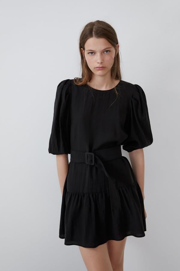 Otra de las versiones en color negro del vestido mini liso de Zara es este de manga abullonada por debajo del codo y bajo acabado en volante. En la cintura se ajusta con un cinturón con hebilla forrada a tono. Cuesta 15,99 euros.