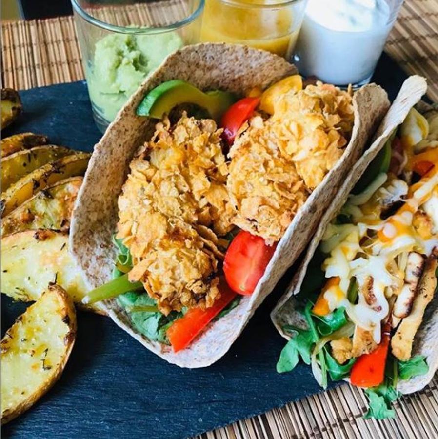 Ingredientes para los tacos:-1 pimiento verde-1/2 pimiento rojo-1/2 cebolla-1/2 zanahoria-1 pechuga de pollo grande-2 cdas salsa soja-1 cdita de mostaza-1 naranja exprimida-Curry, canela, ajo y cebolla en polvo, sal y pimienta al gusto-150 gr copos de maíz sin azúcar-1 huevo (para empanar)-Tortillas integrales-Tomates cherry-Huevos de codorniz, rúcula y canónigos-1 Aguacate-Queso ralladoPreparación:Saltear un poco tiras de pimiento rojo y verde, zanahoria y cebolla.Cortar el pollo a cuadrados y macerarlo con soja, mostaza, zumo de naranja, curry, canela, pimienta, ajo y cebolla en polvo durante un par de horas.La mitad la podéis hacer a la plancha y la otra empanada con cereales sin azúcar, pasándolo por el huevo.Rellenamos las tortillas integrales con añado un poco del salteado, rúcula y canónigos, huevo de codorniz, tomates cherry, aguacate y un poco de queso rallado.Para las salsas:- Guacamole.- Salsa de yogur: yogur griego, sal, pimienta, ajo rallado, perejil y zumo de limón.- Salsa de mostaza y miel: mostaza de Dijon, miel, zumo de limón, sal, pimienta y AOVE.Y para acompañar, unas patatas al horno, cortadas a gajos y especiadas con ajo, cebolla, orégano, tomillo, curry, pimienta y AOVE.