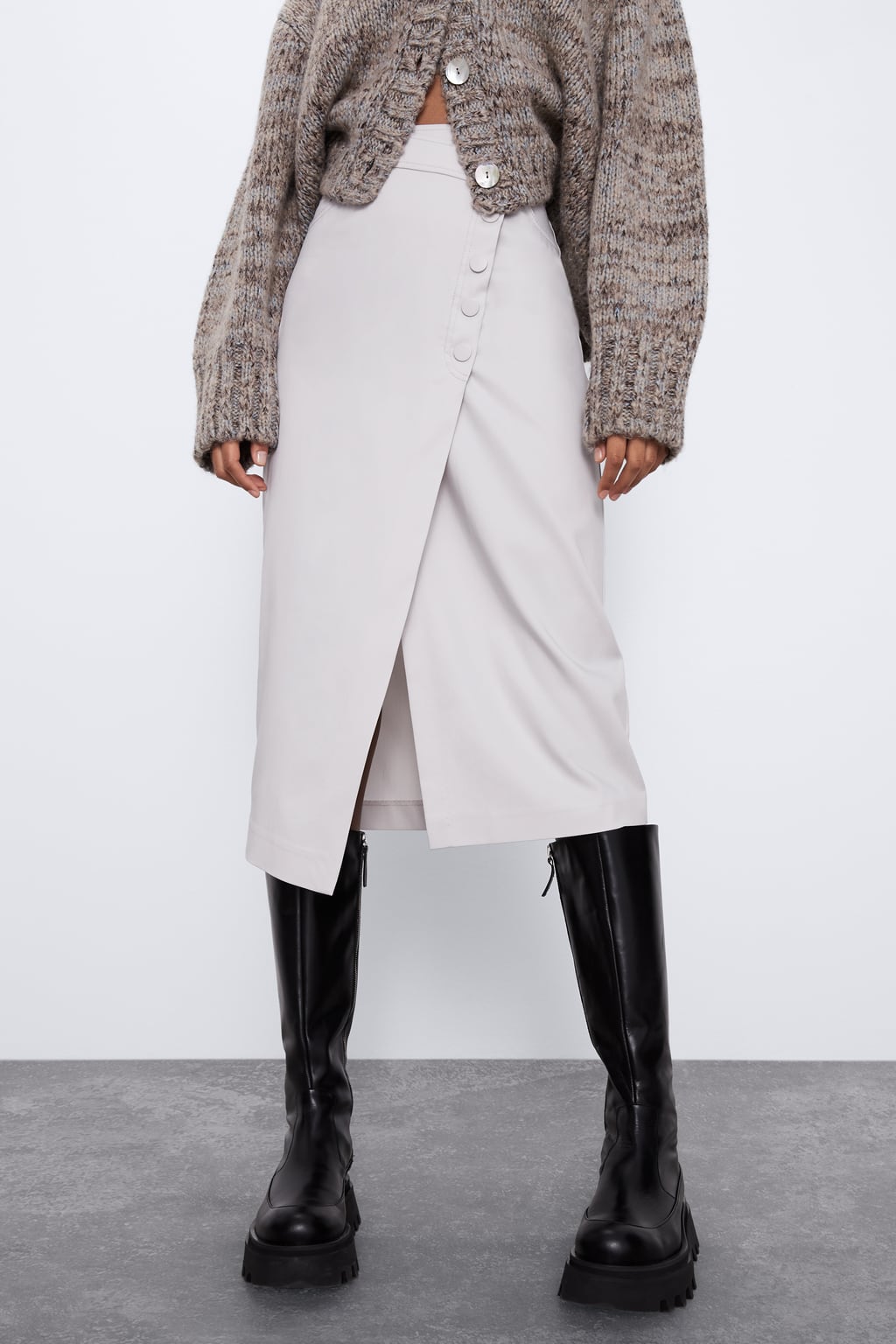 Falda cruzada con cierre de botones en tono crudo de Zara. Nos encanta cómo sienta con estas botas negras de suela track. (25,95 euros).