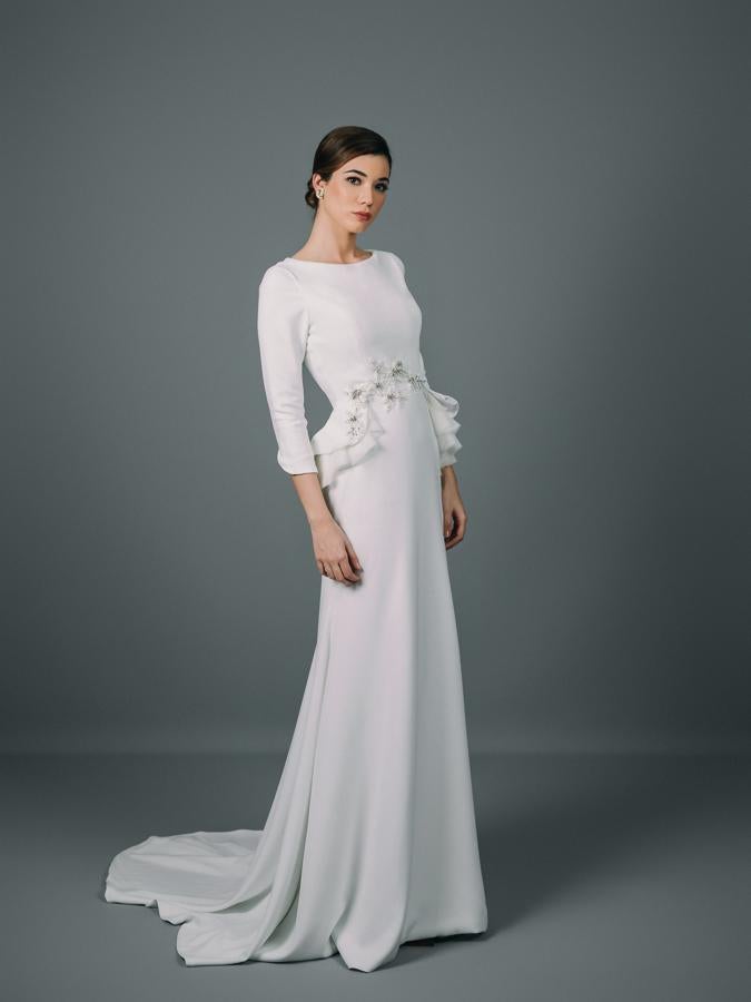 Vestido de novia con corte sirena y cola confeccionada en crepé. Manga francesa y cuerpo entallado con detalle de pedrería y volantes en la cintura. Espalda totalmente abotonada.