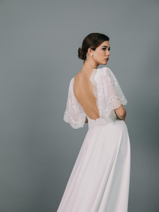 Vestido de novia con mangas de capa y cuerpo entallado confeccionado en gasa bordada.Corte en la cintura y falda de crepé con cola.
