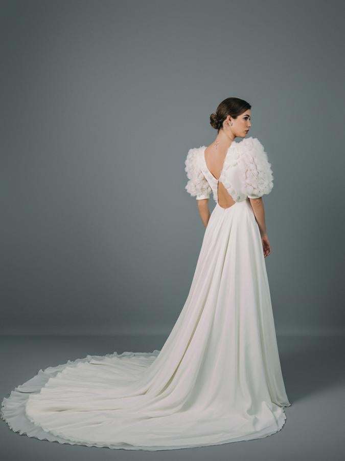 Vestido de novia con cuerpo entallado y escote en forma de lágrima. Voluminosas mangas farol confeccionadas en tejido de tul de fantasía con flores en relieve.Corte en la cintura y falda de capa con cola en tejido de gasa.