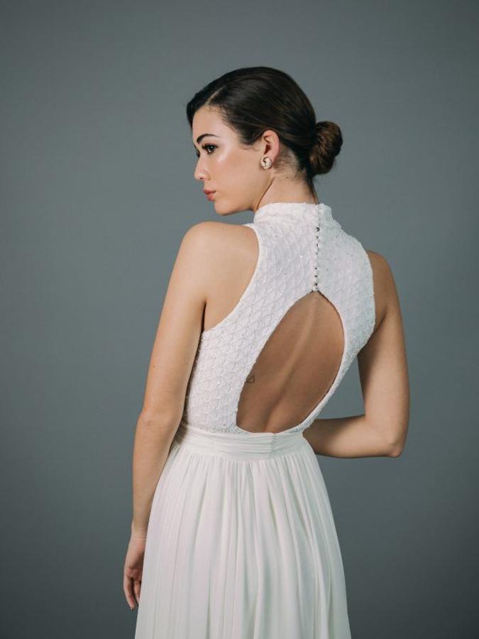 Vestido de novia enterizo de corte recto sin cola confeccionado en pedrería de cristal, con cuello mao. El vestido se complementa con una cola confeccionada en gasa abrochada en la cintura con lazada.