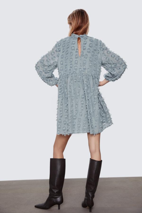 Vestido corto de cuello subido y manga por debajo del codo. Aplicación tejido desflecado combinado a tono. Detalle de pligues en cintura. Incluye forro interior. Cierre en espalda con abertura y botón.